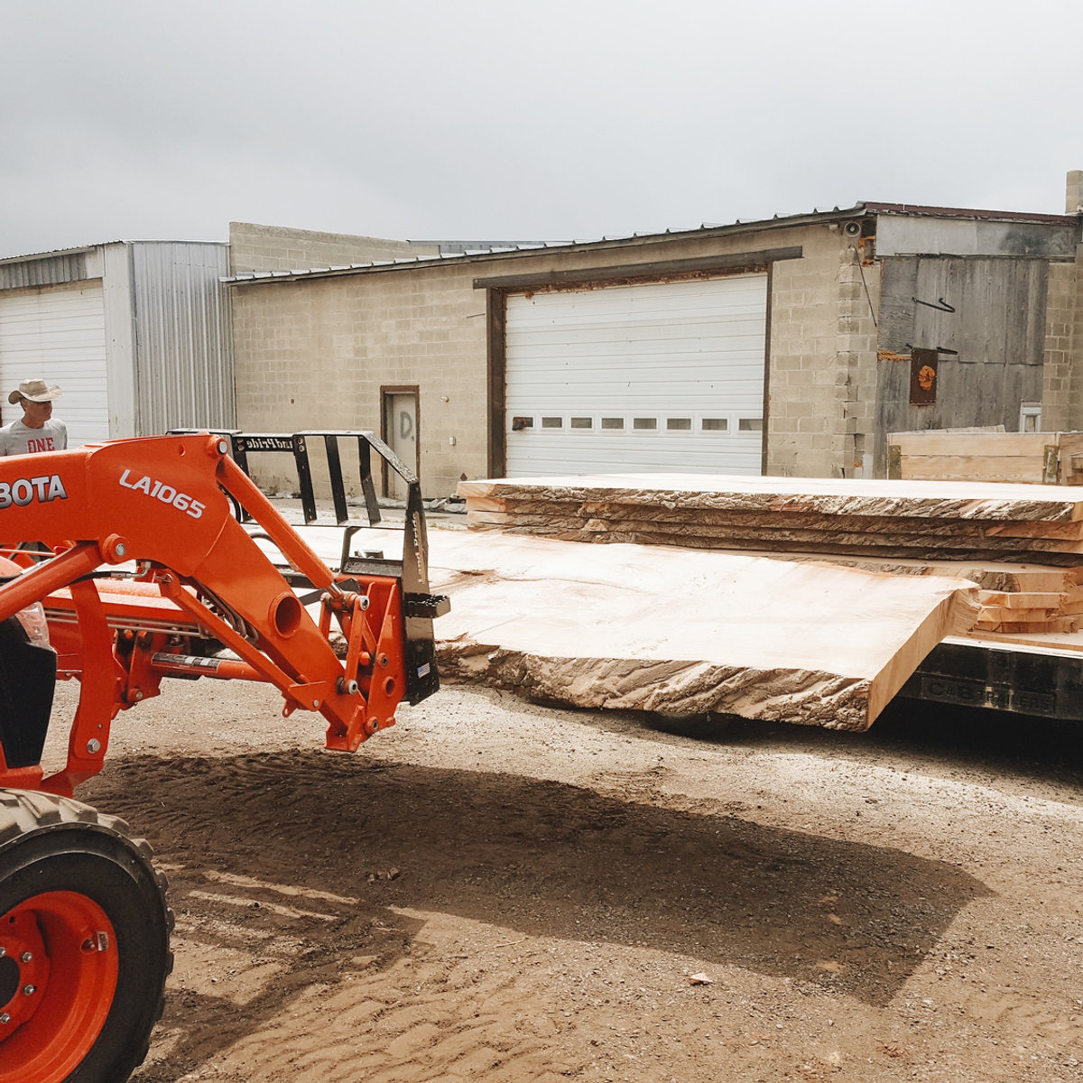 A Kubota loader beside freshly milled slabs on a trailer