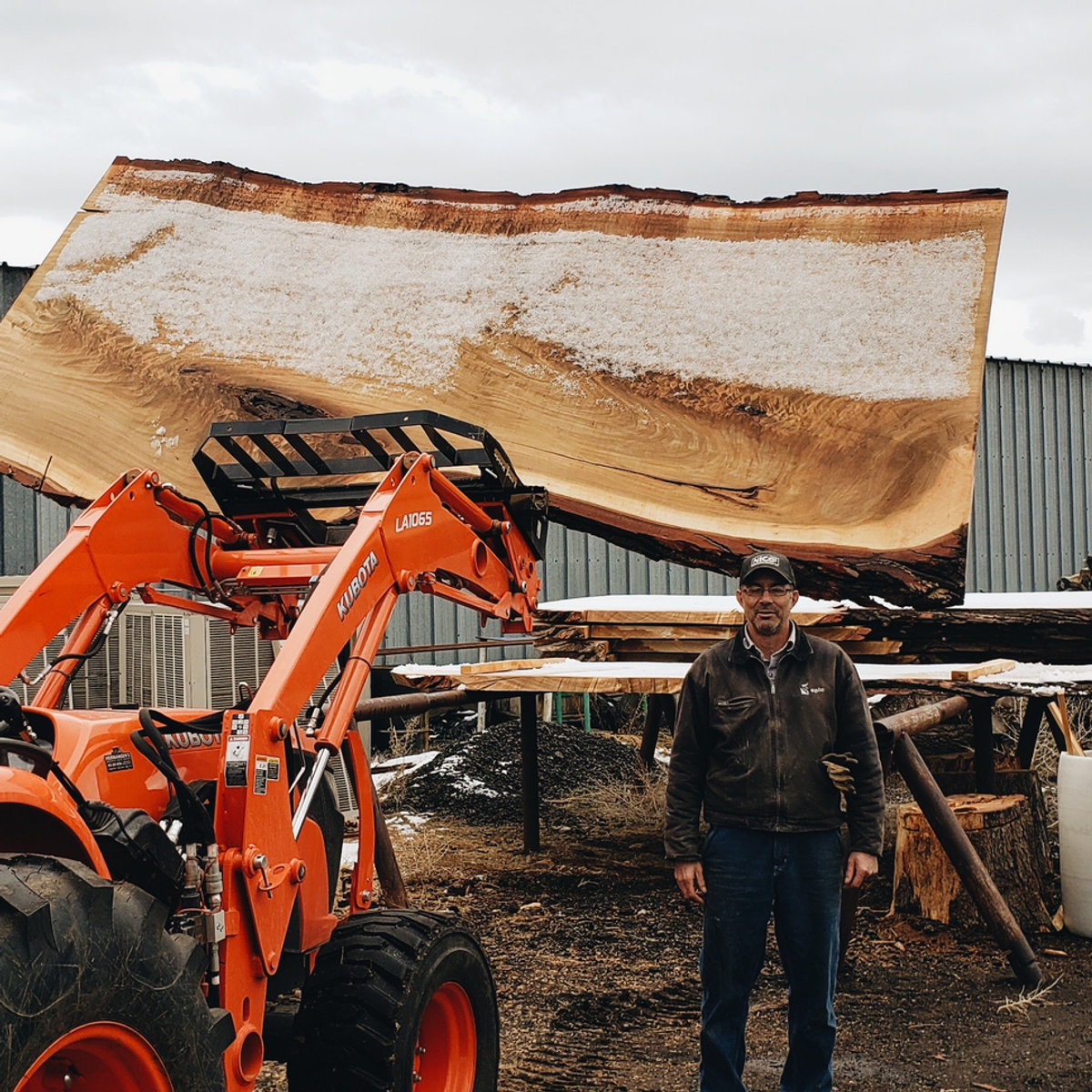 Mark Simons standing in front of a freshly milled live-edge slab held by a Kubota loader